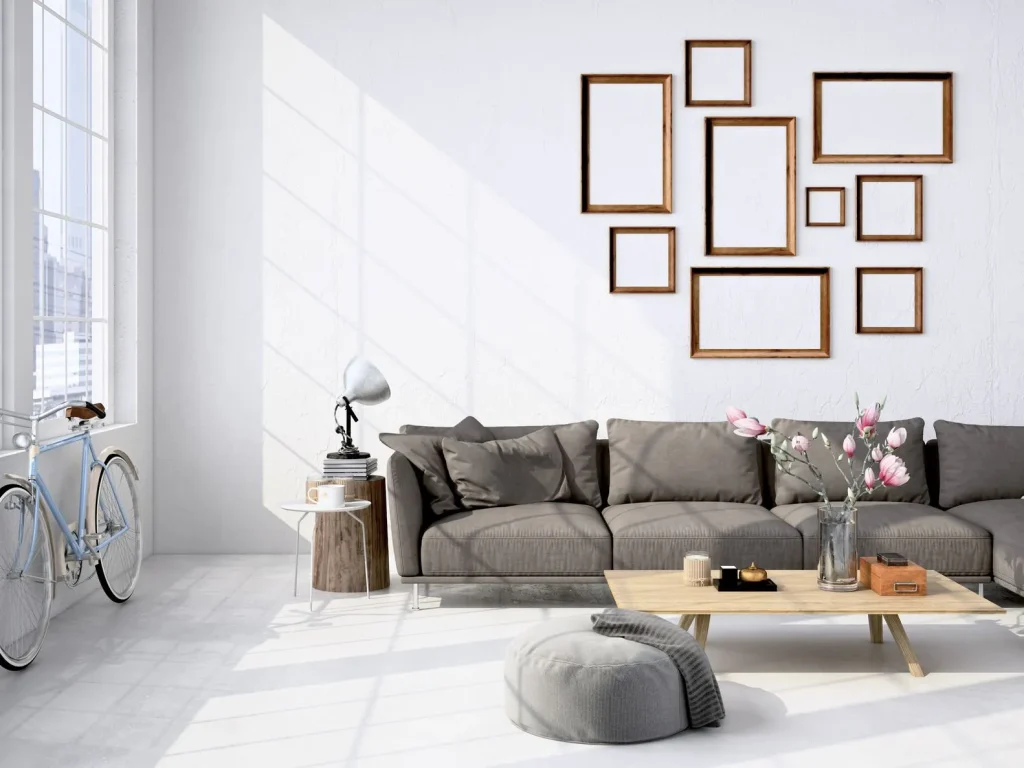 Wohnzimmer: Ein gemütliches graues Sofa vor einer weißen Wand mit leeren Bilderrahmen.