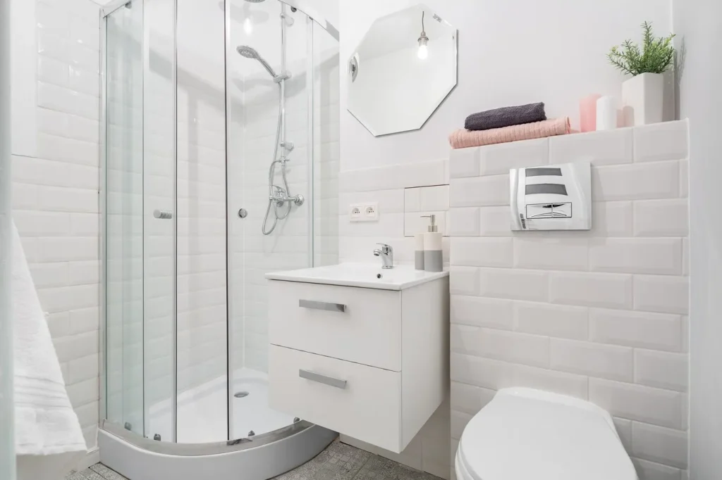 Kompaktes Bad: Ein kleines, weiß gefliestes Badezimmer mit Dusche und WC.